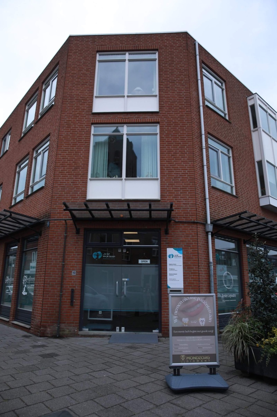 Bakstenen hoekpand aan de Herenstraat in Monster met een glazen entree onder een luifel.